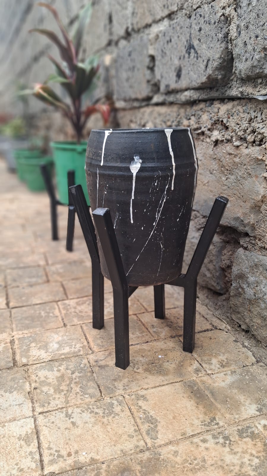 Premium black clay pot with white drip art on black metal stand – front view